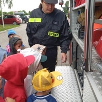 Dzieci i strażak podczas pokazu wyposażenia samochodu straży pozarnej.