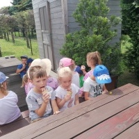 Dzieci siedzą przy stoliku. Jedzą lody. W tle lodziarnia. 