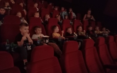 Dzieci siedzą w kinie i zajadają popcorn.