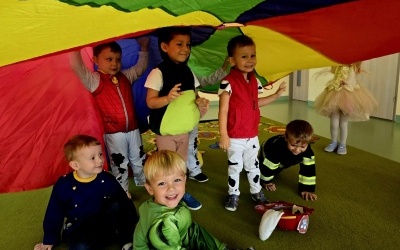 Dzieci w kostiumach bajkowych postaci bawią się chustą animacyjną. 