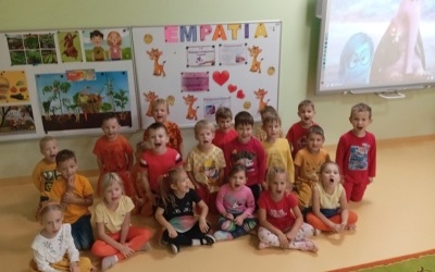 Dzieci ustawione w dwóch rzędach pod tablicą interaktywną pozują do zdjęcia.W tle widoczny napis EMPATIA.