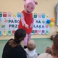 Duża postać świnki Peppy wita się z przedszkolakami. W tle napis na białej tablicy Pasowanie na Przedszkolaka.