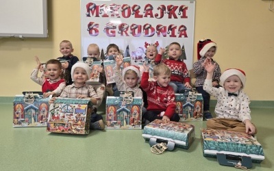 Grupa chłopców pozuje do zdjęcia. W rękach trzymają prezenty od Św. Mikołaja. W tle tablica z napisem MIKOŁAJKI 6 GRUDNIA.