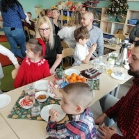 Dzieci razem z rodzicami siedzą przy stole podczas wigilijkowego poczęstunku.