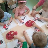 Dzieci siedzą przy stoliku, malują farbą i paluszkami.