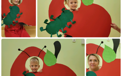 Chłopczyk i dziewczynka oraz dwie nauczycielki pozują jako robaczki w foto budkach w kształcie jabłka.