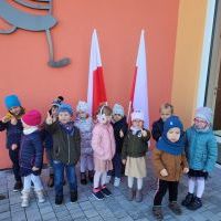 Grupa dzieci stoi ustawiona w jednym rzędzie. W tle dwie flagi Polski. 