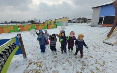 Dzieci w zimowych ubraniach ustawione w rzędzie stoją na placu zabaw.