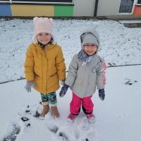 Dwie dziewczynki w zimowych ubraniach stoją na placu zabaw.  