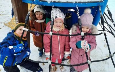 Dwie dziewczynki i dwóch chłopców w zimowych strojach. Stoją pod daszkiem zjeżdżalni.