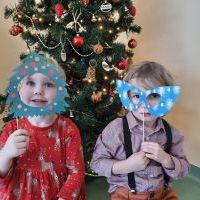 Dziewczynka i chłopiec z gadżetami świąteczno - zimowymi. Za nimi udekorowana choinka.
