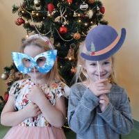 Dwie dziewczynki z gadżetami świąteczno - zimowymi. Za nimi udekorowana choinka.
