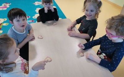 Dzieci siedzą przy stoliku i jedzą ciasteczka w kształcie serca.