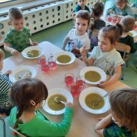 Dzieci siedzące przy stolikach. Zjadają zieloną zupę.