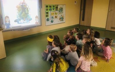 Grupa dzieci siedzi na dywanie i ogląda film edukacyjny dla dzieci pt. 