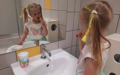 Dziewczynka myje zęby przed lustrem w przedszkolnej łazience. 