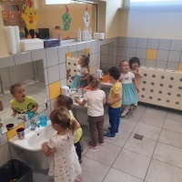 Sześcioro dzieci myje zęby przed lustrem w przedszkolnej łazience. 