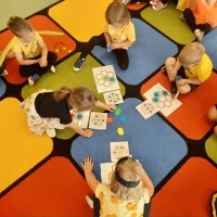 Dzieci siedzące na dywanie układają kolorowe kółeczka na plastrach miodu.