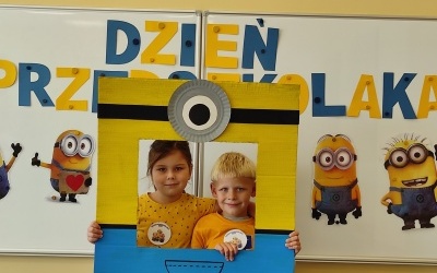 Chłopiec i dziewczynka stoi w fotobudce z minionkiem. W tle tablica z napisem Dzień Przedszkolaka.