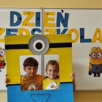 Chłopiec i dziewczynka stoi w fotobudce z minionkiem. W tle tablica z napisem Dzień Przedszkolaka.