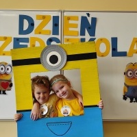 . Dwie dziewczynki stoją w fotobudce z minionkiem. W tle tablica z napisem Dzień Przedszkolaka.