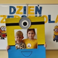 Chłopiec i dziewczynka stoi w fotobudce z minionkiem. W tle tablica z napisem Dzień Przedszkolaka.