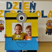 Dwóch chłopców stoi w fotobudce z minionkiem. W tle tablica z napisem Dzień Przedszkolaka.