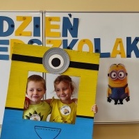 Chłopiec i dziewczynka stoi w fotobudce z minionkiem. W tle tablica z napisem Dzień Przedszkolaka.