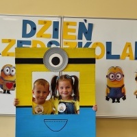 Chłopiec i dziewczynka stoi w fotobudce z minionkiem. W tle tablica z napisem Dzień Przedszkolaka.