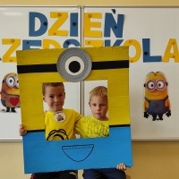 Dwóch chłopców stoi w fotobudce z minionkiem. W tle tablica z napisem Dzień Przedszkolaka.