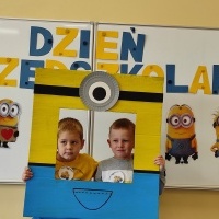 Dwóch chłopców stoi w fotobudce z minionkiem. W tle tablica z napisem Dzień Przedszkolaka.