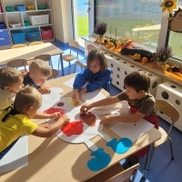 Grupa chłopców siedzi przy stoliku i maluje farbami.