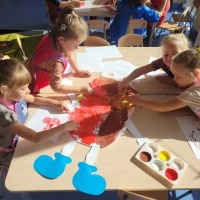 Grupa dziewczynek siedzi przy stoliku i maluje farbami.