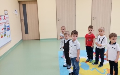 Dzieci stojące przodem do godła , ustawione w rzędach i śpiewające hymn Polski. 