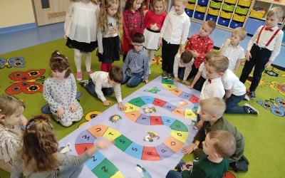 Dzieci na dywanie oglądają matę edukacyjną.