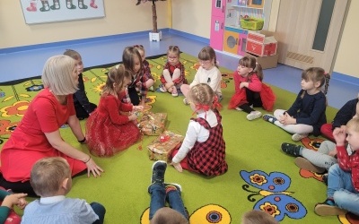 Dzieci siedzą na kolorowym dywanie i rozpakowują prezenty.