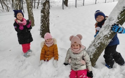 Dzieci pozują do zdjęcia na śniegu w kombinezonach. 