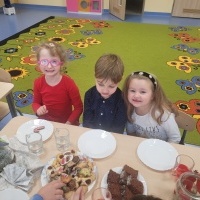 Dwie dziewczynki i chłopczyk siedzą przy stole udekorowanym świątecznymi dekoracjami i ciasteczkami. 