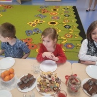 Grupa dzieci siedzi przy stole. Na stole ustawione talerze z ciastkami i dekoracje świąteczne.