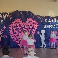 Dziewczynki wykonują taniec z okazji Dnia Babci i dziadka. W tle dekoracja z różowych motylków.