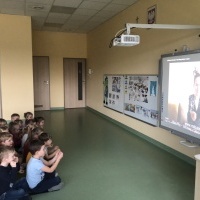Dzieci siedzą na dywanie, obserwują film z językiem migowym.