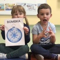 Dziewczynka trzyma w ręku obrazek z bombką, obok siedzi chłopiec miga znak 
