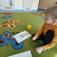 Chłopczyk siedzi na dywanie i układa plasterki ogórków na kartce.