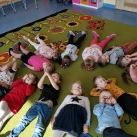 Dzieci leżą na dywanie na plecach i odpoczywają. 