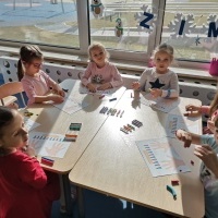 Grupa dzieci siedzi przy stoliku. Dzieci tworzą prace plastyczne.