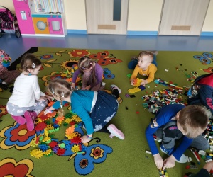 Grupa dzieci siedzi na dywanie i buduje z klocków lego.