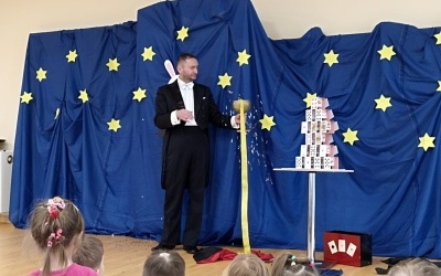 Iluzjonista prezentujący magiczne sztuczki. Dzieci zwrócone do niego twarzami.