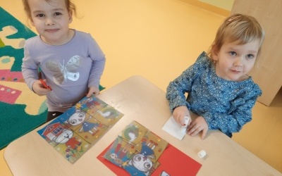 Dwie dziewczynki przy stoliku wykonują pracę plastyczną typu puzzle.