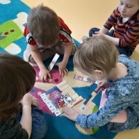 Czworo dzieci układa Kiciowe puzzle na dywanie.