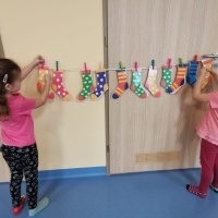 Dziewczynki przyczepiają kolorowe skarpetki na sznurek za pomocą klamerek.